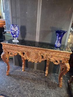 The Baroque-style console features a dark marble top and a carved wood base with a gold-leaf finish.