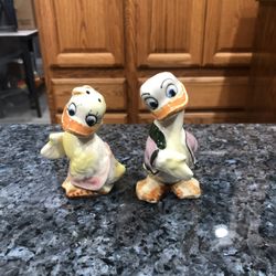 Ceramic Vintage Donald Duck and Daisy Duck pair of salt and pepper shakers shaking hands.  Only one has a cork stopper.  