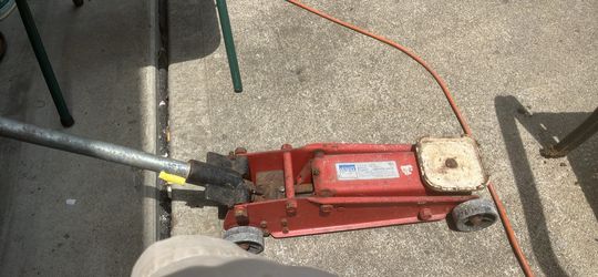 This red hydraulic floor jack resembles models from brands like Norco or Montgomery Ward, typically with capacities ranging from 1.5 to 3 tons.