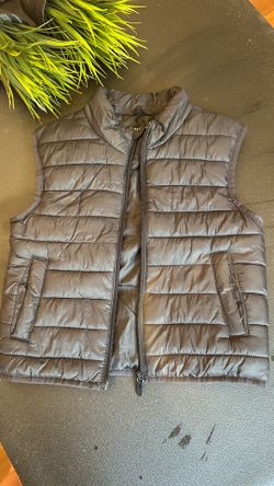 Kids sleeveless quilted puffer vest. Front zip closure with snap detail. Simple branded interior print. Solid black color for easy styling.