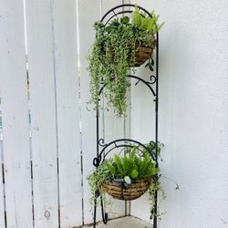 A tall sturdy iron plant stand with two baskets of plants