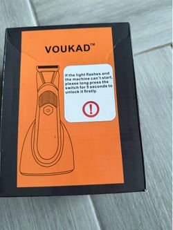 New VOUKAD groin and body hair trimmer is black with an orange and black box. This electric trimmer has a charging stand and a safety lock feature.