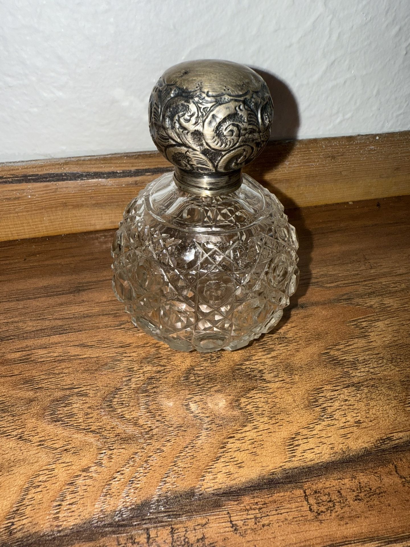 An antique cut crystal or glass perfume bottle with a sterling silver or silver-plated top, The glass body features a hobnail cut or faceted pattern.