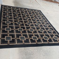 Durable rug with a modern geometric pattern. Has interconnected squares and lines in black, brown, and tan colors