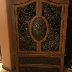 French-style armoire or entertainment cabinet featuring intricate woodwork decorative panels, a rich wood finish, and multiple storage drawers.