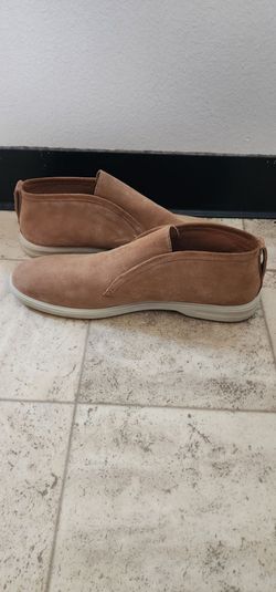 The shoe shown is the Peter Millar Crown Crafted Excursionist Chukka in a tan suede finish, featuring an innovative laceless slip-on design.