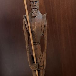 A tall, slender, hand-carved wooden sculpture of a person holding a long staff or spear., $15