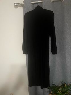 Elegant black midi dress has a turtleneck and long sleeves. The material is a soft knit with ribbed cuffs at the wrists. It is a solid black color thr