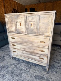 This vintage-style armoire features a whitewashed finish and distinct brass hardware pulls.