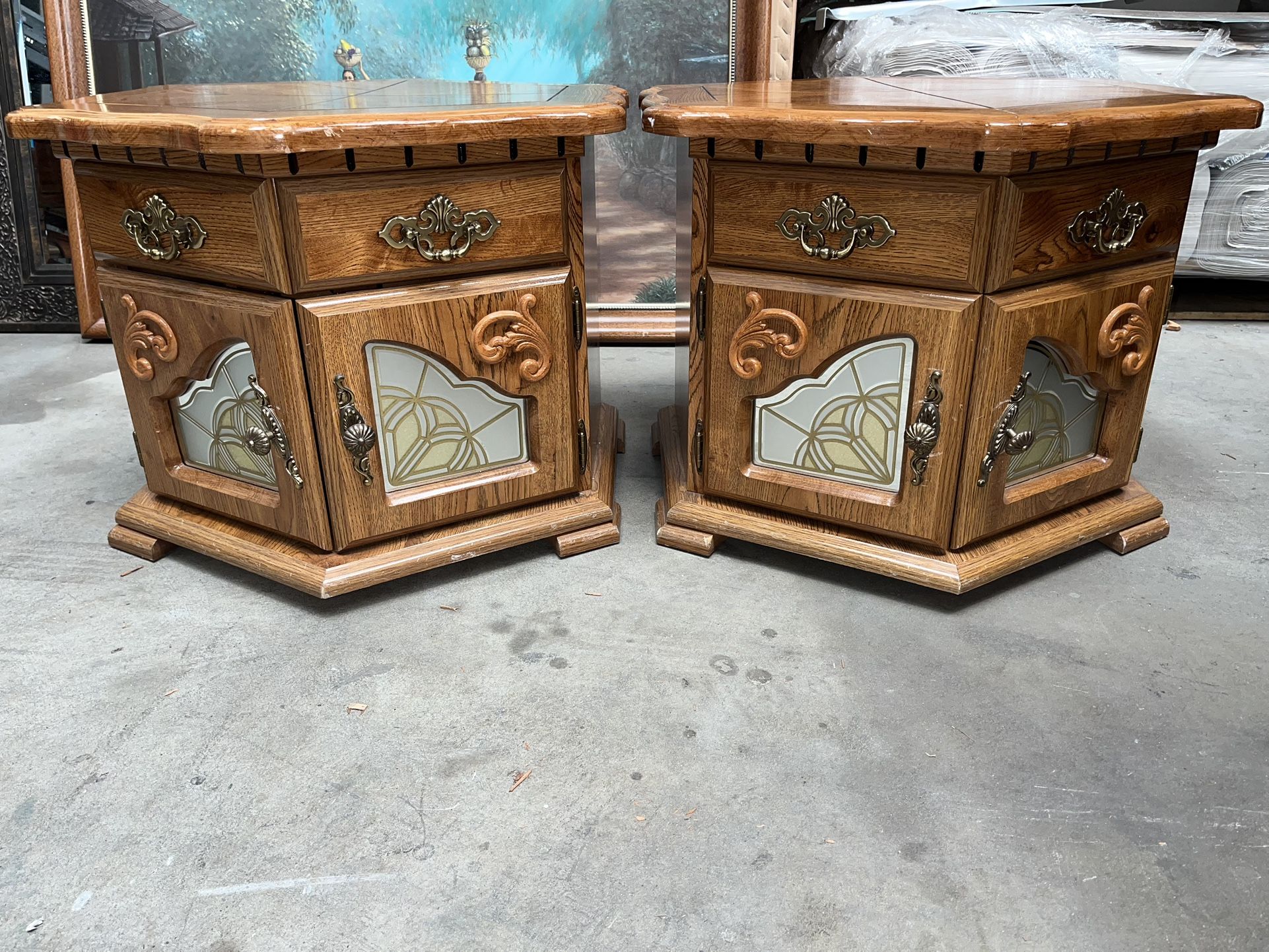 pair of oak end tables with a drawer and a cabinet featuring a stained-glass-style panel