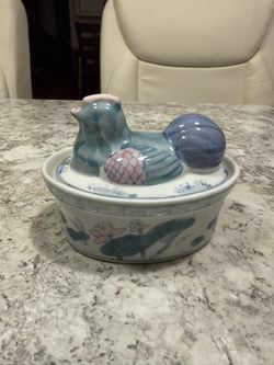 This is a vintage hand-painted Chinese porcelain hen on a nest lidded trinket box, decorated in blue, green, and pink with lotus flowers around the ba