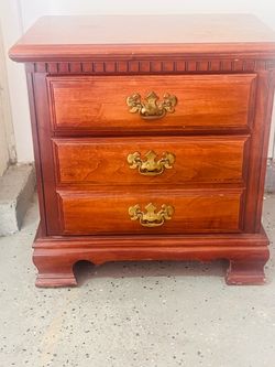 A vintage three-drawer cherry nightstand with traditional brass bail handles and dentil molding.