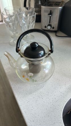 clear glass stovetop teapot/tea kettle featuring a painted white and yellow daisy floral motif on the side.