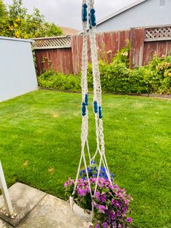Colorful macrame hanging planter has white braided cord and blue beads. Pot of Flowers Are not included.