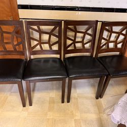 four wooden chairs, each with a unique lattice-style backrest design. The seats are upholstered in black leather, providin
