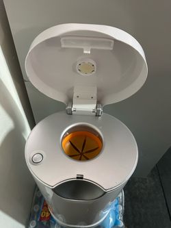 White Munchkin Arm & Hammer diaper pail with a silver top and orange odor-sealing ring. This plastic unit has a foot pedal for hands-free operation an
