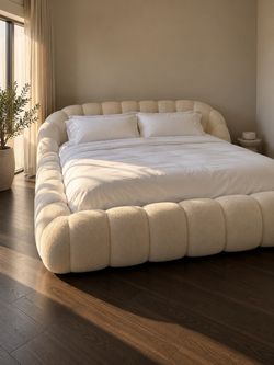 California King ivory bouclé upholstered cloud bed, featuring a sculptural, oversized, channel-tufted frame.