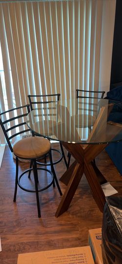 Glass table top with wooden pedestal base includes three barstool chairs