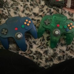 These are Nintendo 64 (N64) controllers, with one in a solid blue color and the other a transparent green
