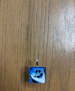 Necklace with a square pendant with an image of a hand holding a blue buttterfly