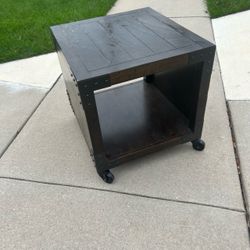 Nice dark wood & metal end table 23.5”T 22”W 24”D with a lower open shelf on caster wheels