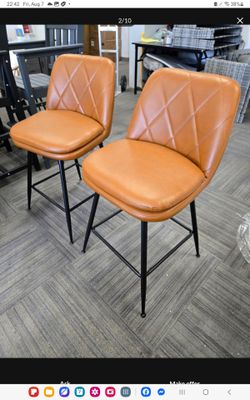 Modern swivel bar stools have saddle brown PU leather upholstery with diamond-patterned stitching. Each stool is constructed with a black metal frame 
