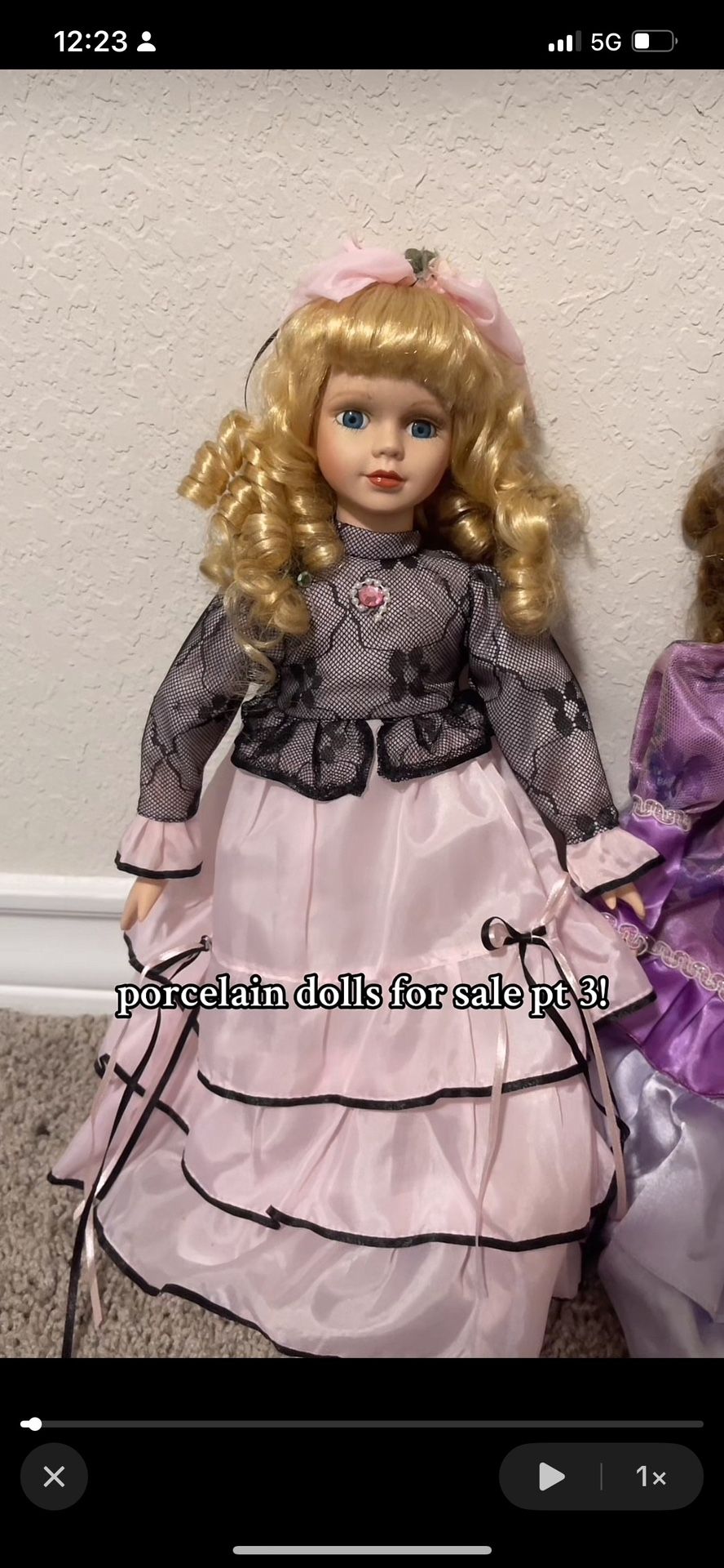 vintage antique porcelain doll with stand, blonde curls, blue eyes, and a black and pink dress