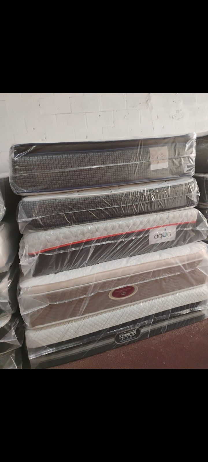 Have All Size Available Good Prices Todos Los tamaños Disponibles Stack of new mattresses wrapped in protective plastic. Multiple styles available.