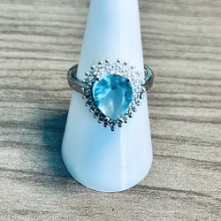 Elegant silver ring featuring a teardrop blue crystal center. Sparkling halo detail enhances the vibrant blue stone. Comfortable band with a polished 
