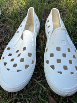 White Vans Slip-On TRK shoes are size US 13. The shoes have a molded synthetic construction with cutout square patterns. Preowned in good condition