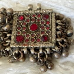 This is a vintage Kuchi Afghan tribal prayer box pendant featuring red glass stones and small bells.