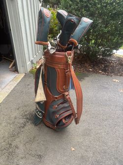 Vintage Daiwa Coach Collection golf bag in classic brown leather and dark green canvas. Features the signature brass carriage/rickshaw logo plaque on