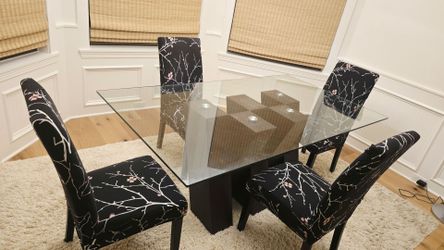 Dining table with glass top and dark wooden base with 4 fabric cushion chairs
