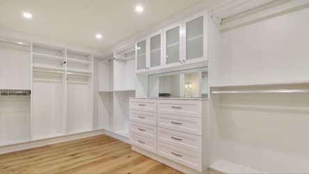 Master Walk-In White Closet with Raised Panel Drawer Fronts, Glass Upper Doors with a Mirror Above the Two Chests of Drawers. Everything is adjustable