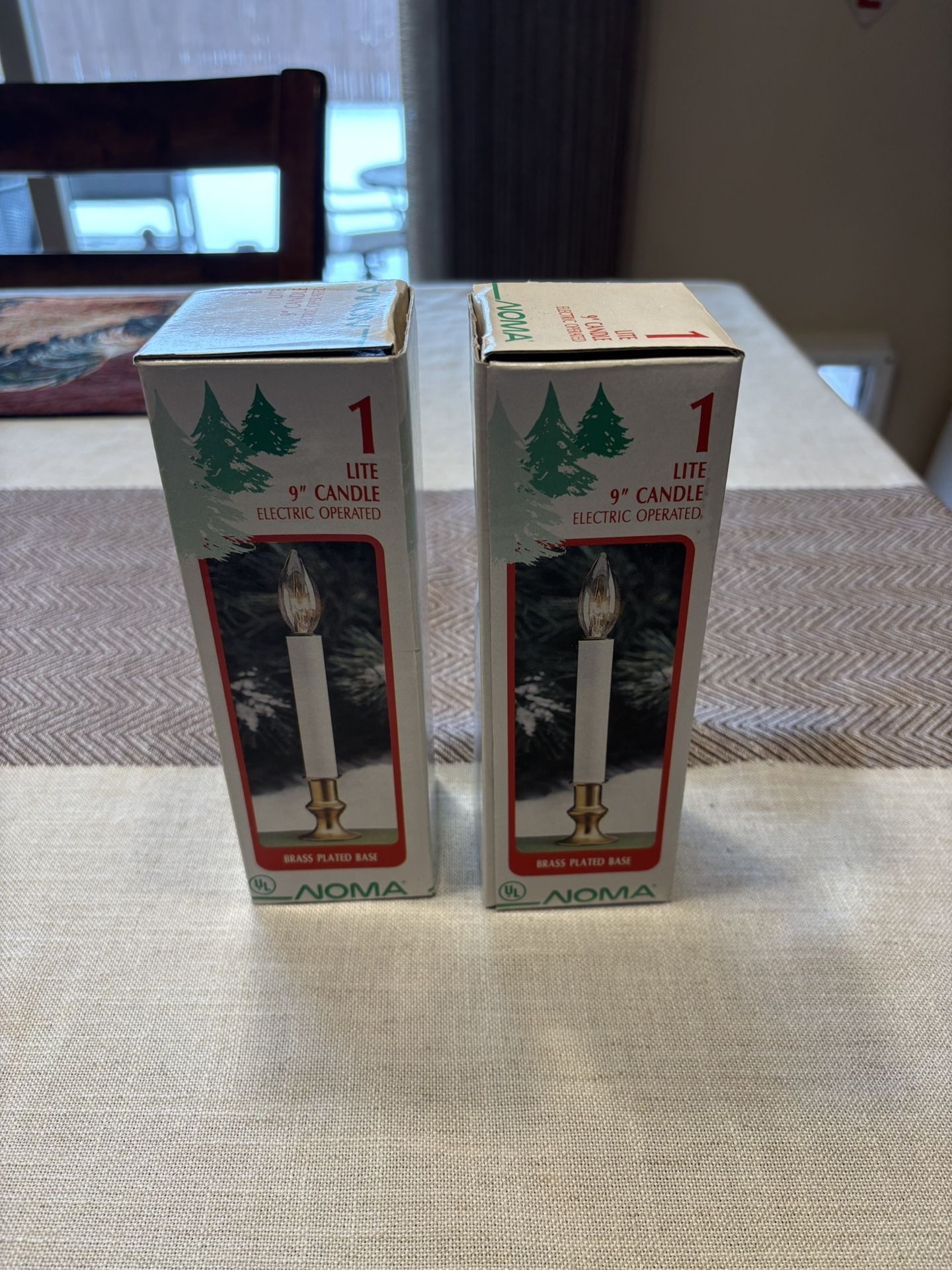Two boxes of NOMA brand 9-inch electric window candles with brass-plated bases.