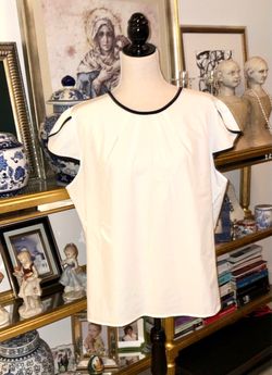 White blouse with a round neck that stands out for its elegant black trim details on the neck and flared sleeves.