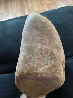 Based on its smooth, rounded texture and reddish-brown coloration, this specimen is likely a river stone composed of quartzite, sandstone, or jasper.