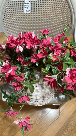 Artificial pink flowered plant in white wicker basket.