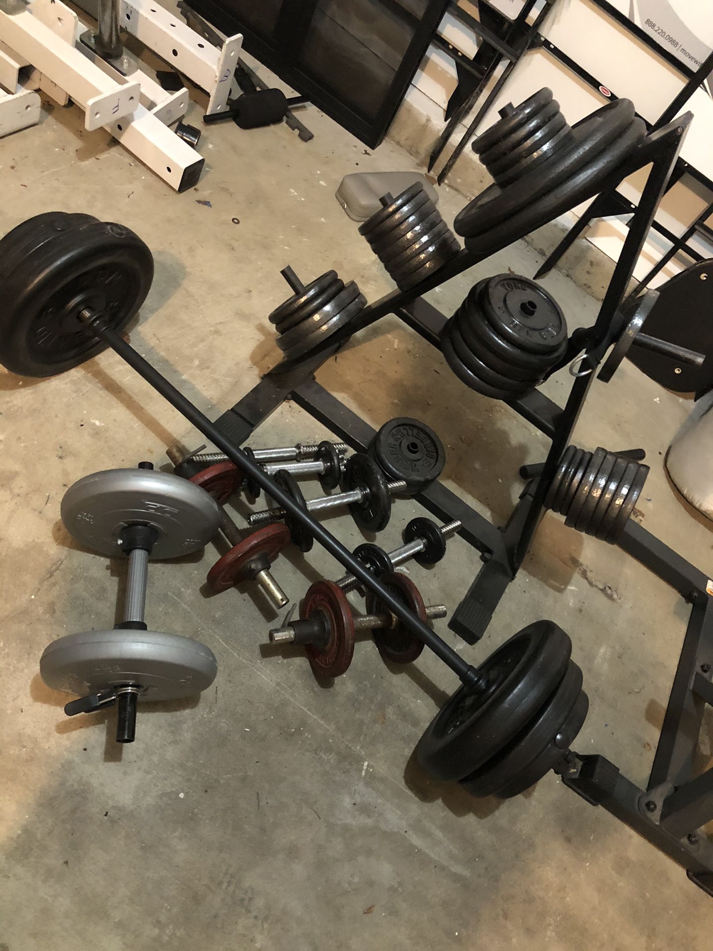 Set of different size Standard weight plates with weight tree, barbell with weights, few dumbbells and dumbbell handlebars. Total weight is more than