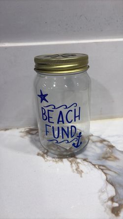 Cute “Beach Fund” 5”1/2 inches tall mason jar saving bank, blue lettering with gold toned lid.