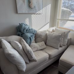 Beige Two Seater Sofa & Ottoman w/ Pillows & Wall Decor