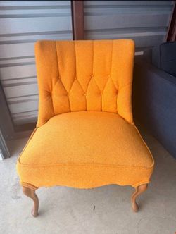 This vintage-style orange upholstered slipper chair features a button-tufted, diamond-patterned back