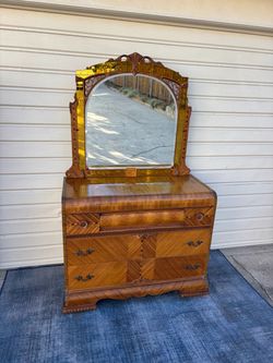 Vintage Art Deco waterfall dresser with an attached arched mirror featuring amber-tinted glass panels and geometric wood inlay on casters