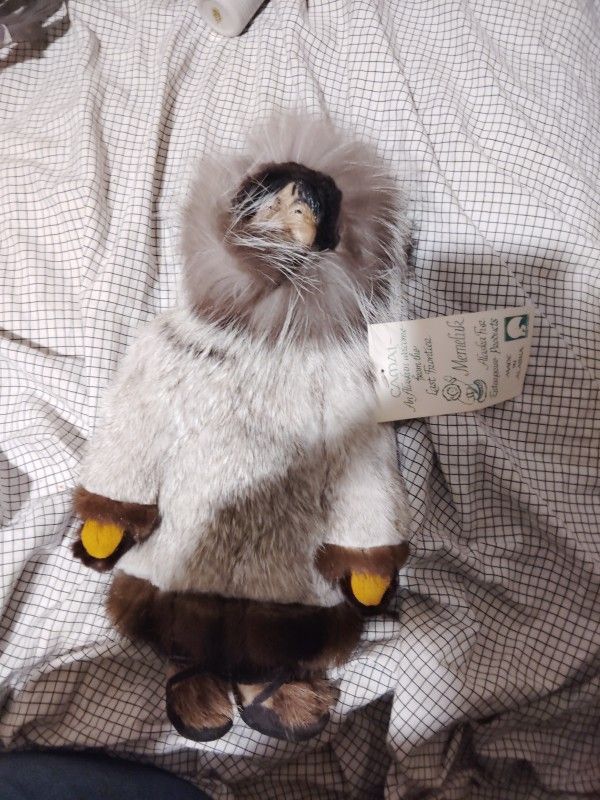 Nooak Alaskan Camai, The doll has a plush fur lined body and resin face. The doll is wearing a multi colored hooded coat made of fur with matching fur