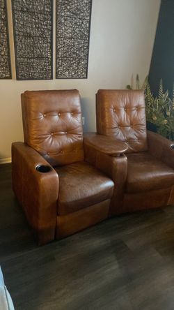 This is a caramel-colored leather home theater reclining loveseat featuring button-tufted backrests and an integrated center console with a swivel tab