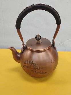 Handmade, uncoated red copper tea kettle or teapot with Chinese script embossed on the body, a woven-wrapped high arch handle, and a matching lid with