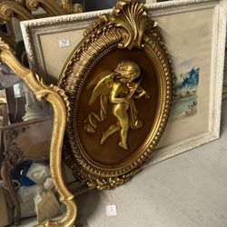 Gilded relief cherub playing violin wall plaque in ornate frame.