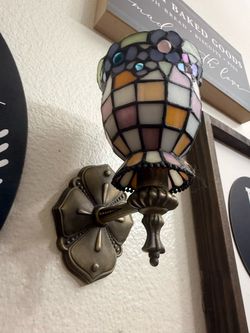 PartyLite Hydrangea wall sconce features a Tiffany-style stained glass votive cup with a pastel floral mosaic pattern and an antique brass finish meta