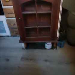 

This is a vintage wooden wall-mounted display or curio cabinet with a glass door 