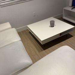 Sala blanca en L, mesa de centro blanca y escritorio con silla